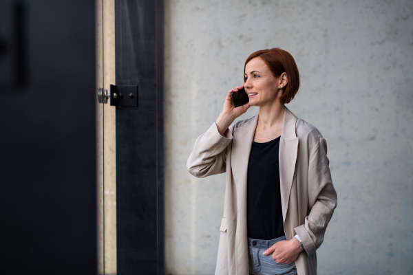 A portrait of mid adult businesswoman standing indoors, using smartphone.