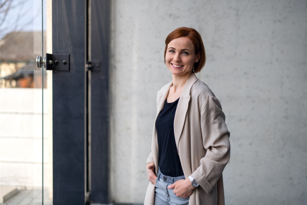 A portrait of mid adult businesswoman standing indoors, looking at camera.