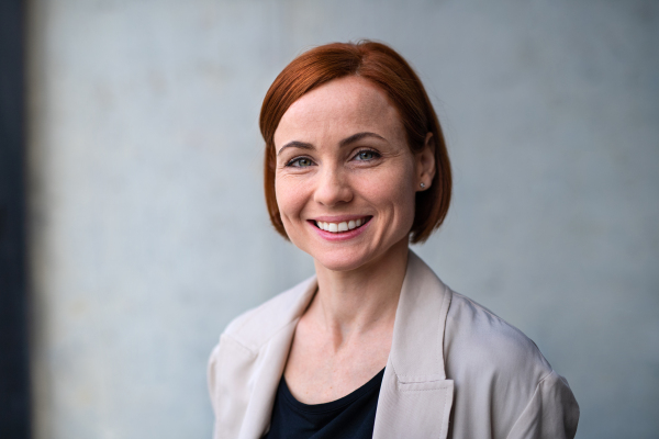 A portrait of mid adult businesswoman standing indoors, looking at camera.