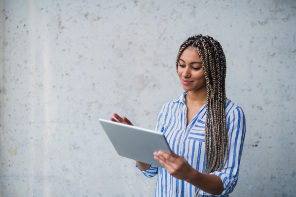 A portrait of young woman freelancer standing indoors, using tablet.