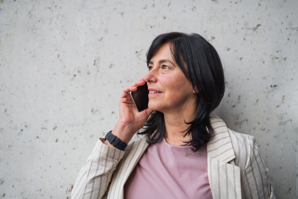 A portrait of senior businesswoman standing indoors, using smarpthone.