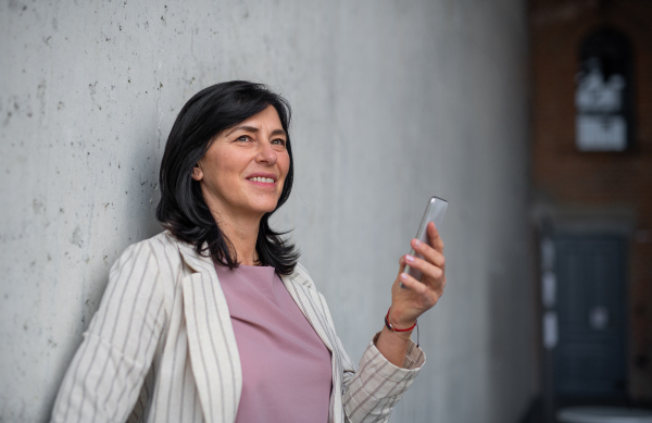 A portrait of senior businesswoman standing indoors, using smarpthone.