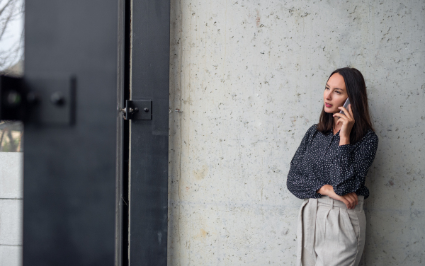 A portrait of mid adult businesswoman standing indoors in office, using smartphone.