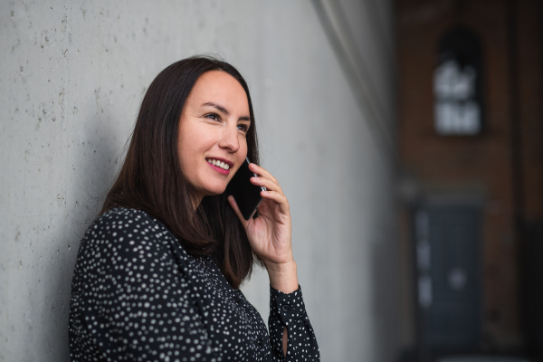 A portrait of mid adult businesswoman standing indoors in office, using smartphone.