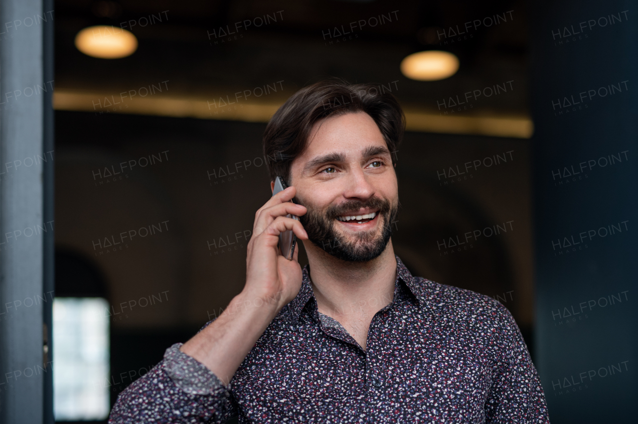 A portrait of young businessman standing indoors, using smarpthone.