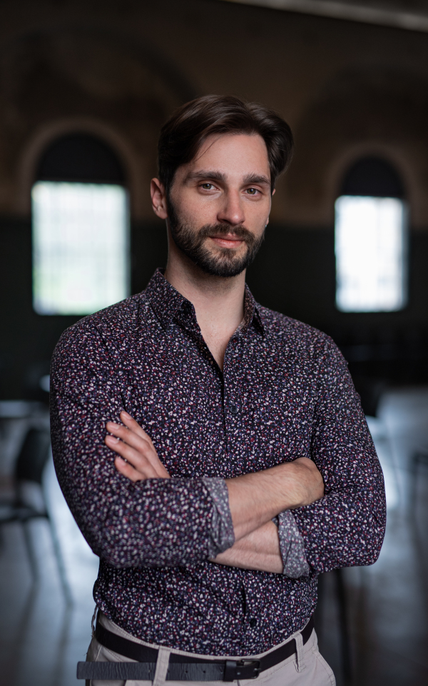 A portrait of young businessman standing indoors in office, looking at camera.