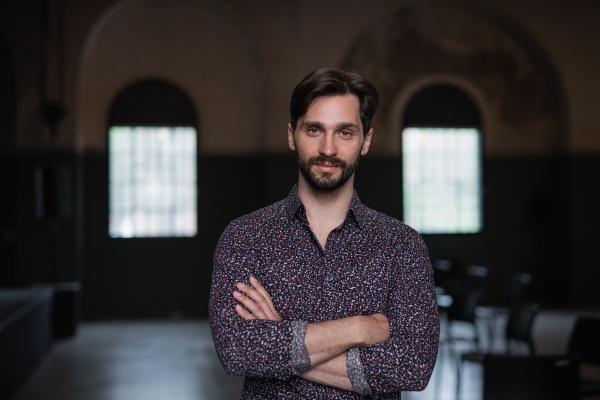 A portrait of young businessman standing indoors, looking at camera.