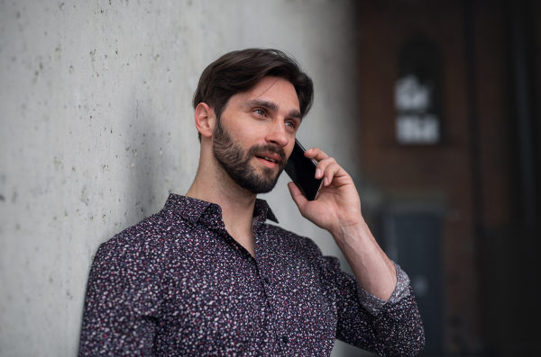 A portrait of young businessman standing indoors, using smarpthone.