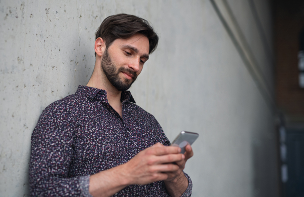 A portrait of young businessman standing indoors, using smarpthone.