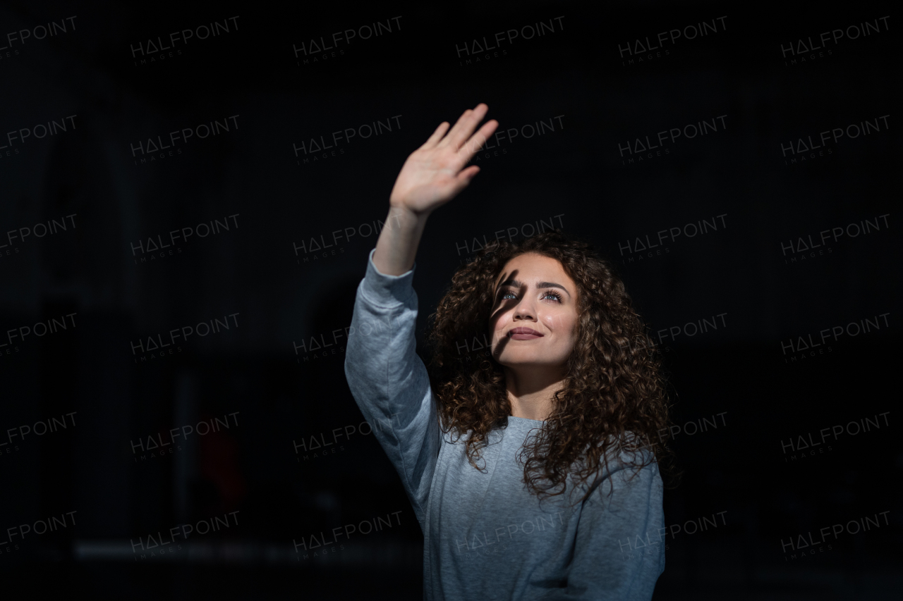 A portrait of young woman standing indoors against black bacground, playing with shadow.