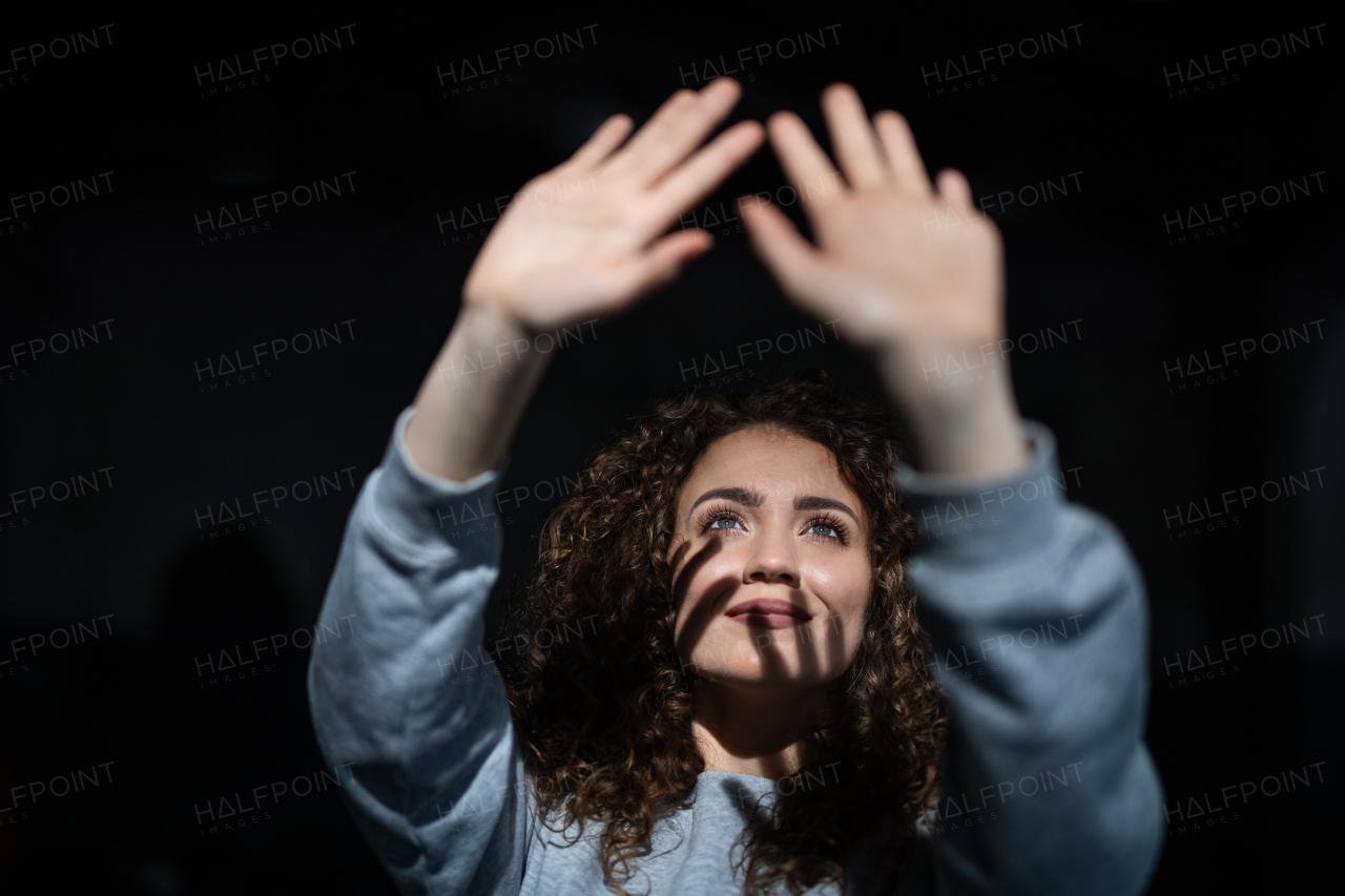 A portrait of young woman standing indoors against black bacground, playing with shadow.