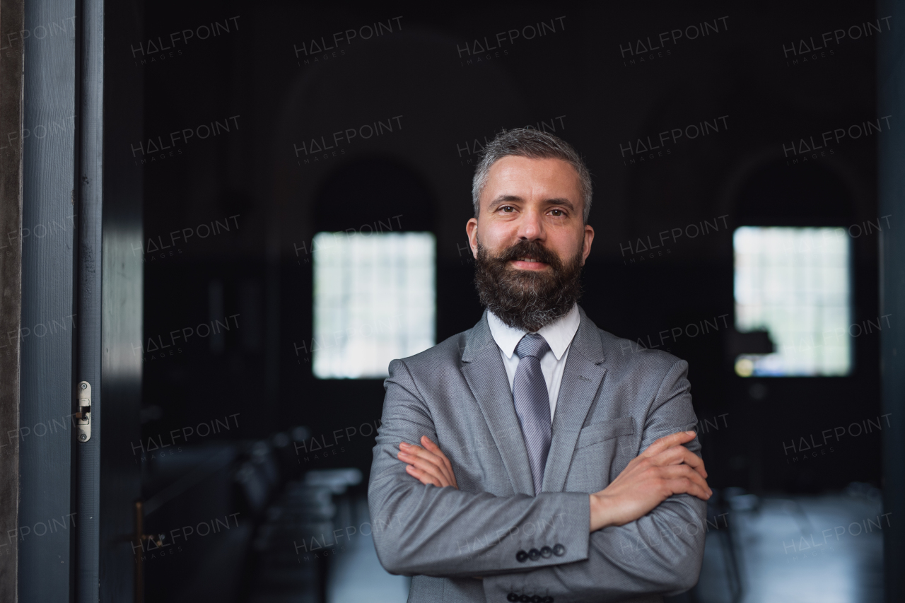 A portrait of young businessman standing indoors, looking at camera.