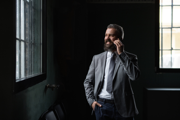 A portrait of mature businessman standing indoors, using smartphone.