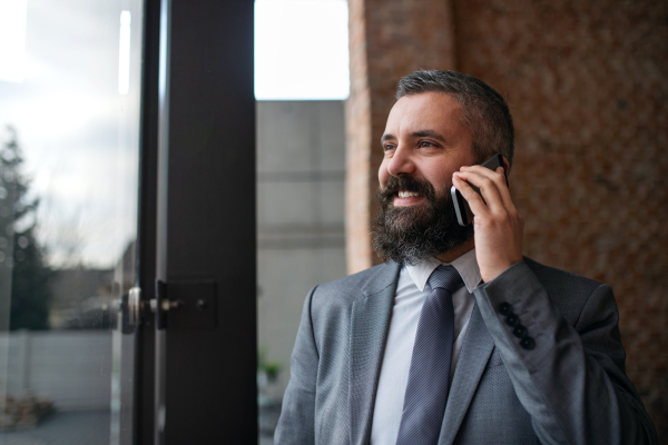 A portrait of young businessman standing indoors, using smartphone.