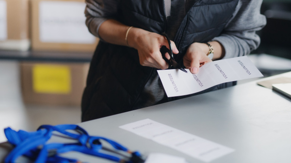 Unrecognizable woman volunteer working in community charity donation center, cutting labels.