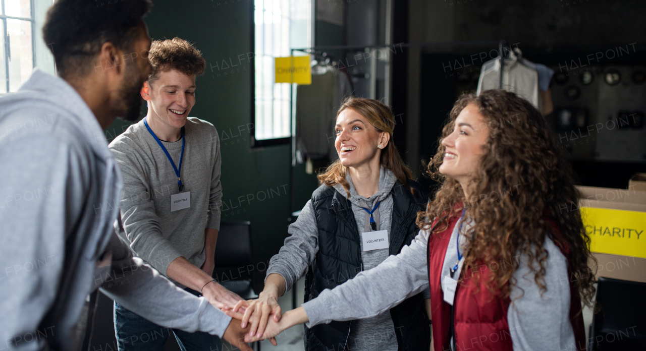 A group of volunteers at work in community charity donation center, stacking hands together.