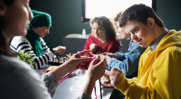 Group of happy people playing cards and board games in community center, inclusivity of disabled person.