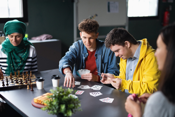 Group of happy people playing cards and board games in community center, inclusivity of disabled person.