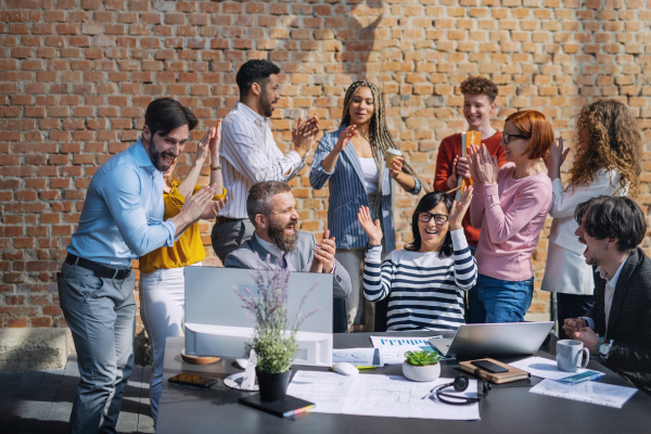 A group of excited entrepreneurs working on project indoors in office, celebrating successful contract.