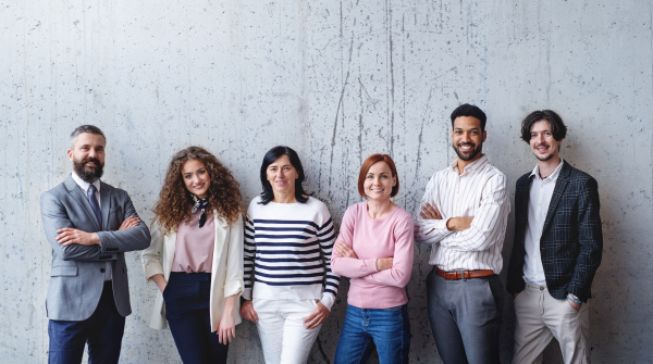 Front view portrait of group of entrepreneurs standing against concrete wall indoors in office, looking at camera.