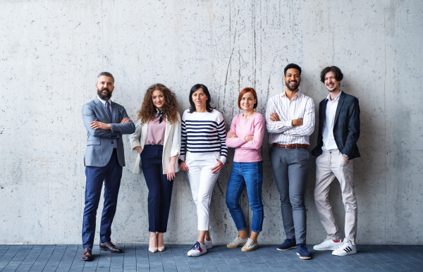 Front view portrait of group of entrepreneurs standing against concrete wall indoors in office, looking at camera.