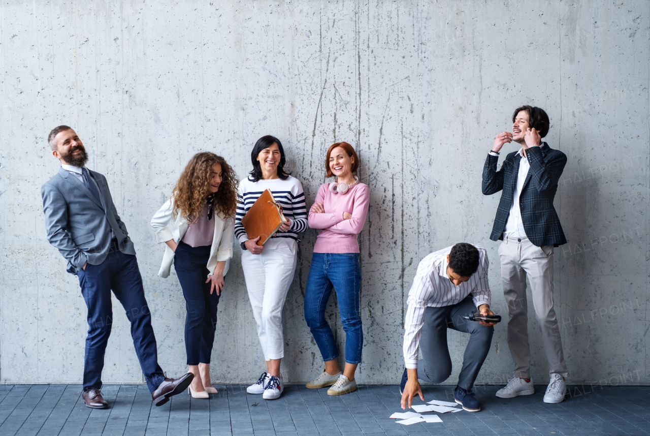 Front view portrait of group of entrepreneurs standing against concrete wall indoors in office, laughing.