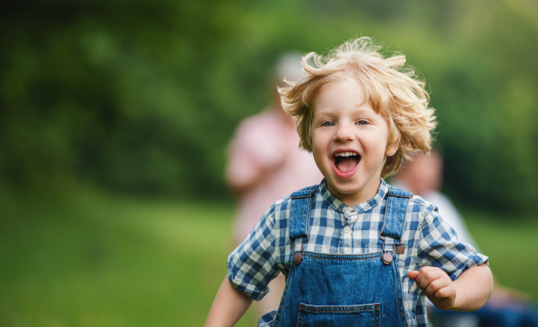 Portrait of small boy with unrecognizable grandparents on a walk on meadow in nature, running.