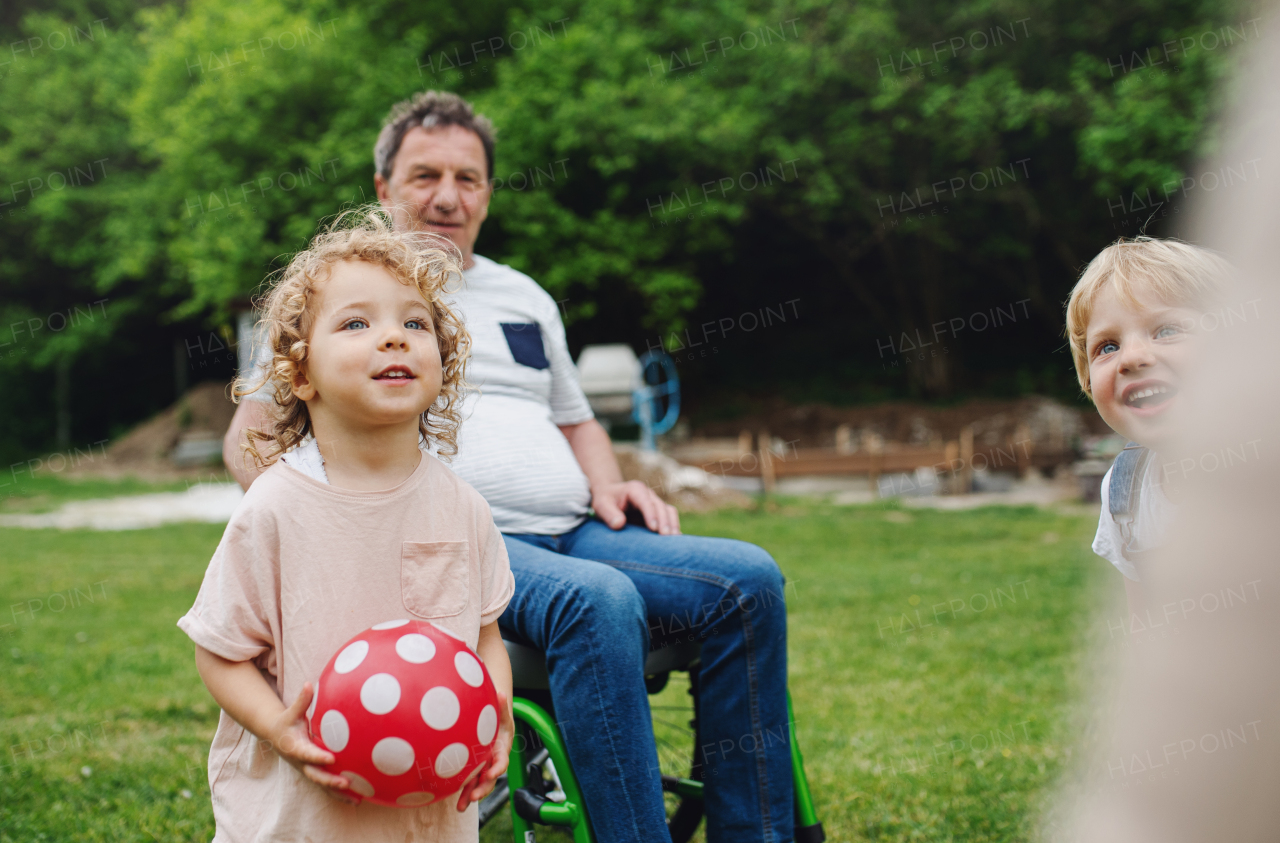 Happy small children with senior grandparents in wheelchair playing.