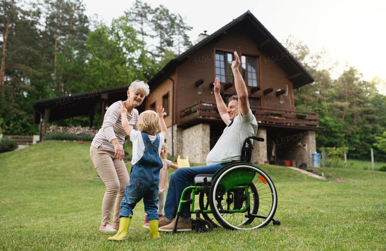 Happy small children with senior grandparents in wheelchair playing.