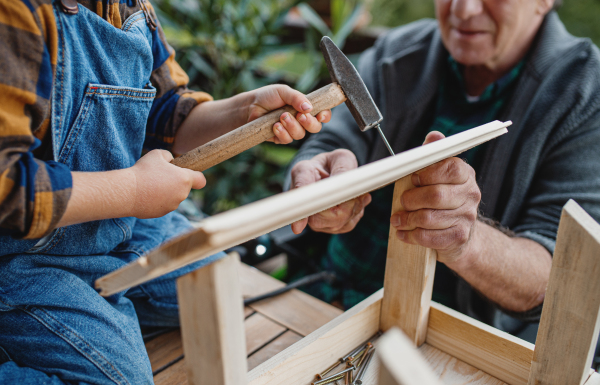 Midsection of unrecognizable small boy with senior grandfather constructing birdhouse, diy project.