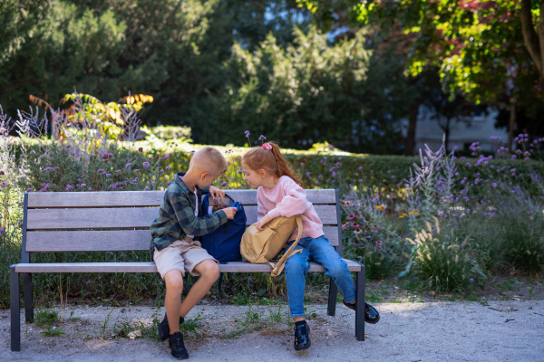 A happy kids sitting on bench outdoor in park , talking and preparingand homework.