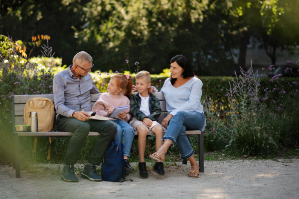 A senior couple with grandchildren sitting on bench and doing homewrok outdoors in park.