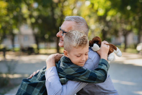 A happy little boy hugging his grandfather outdoors in park.