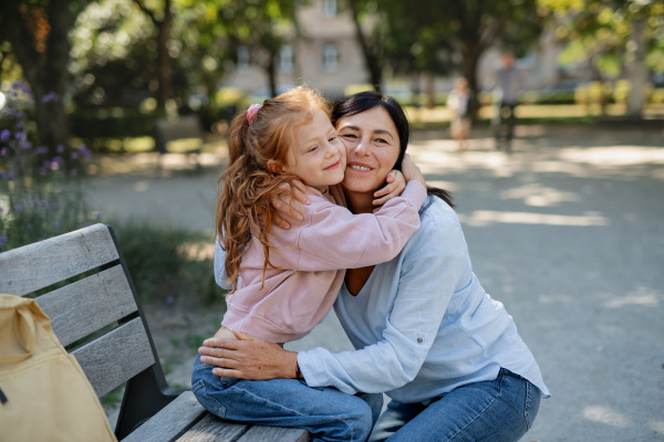 A happy little girl hugging her grandmother outdoors in park.