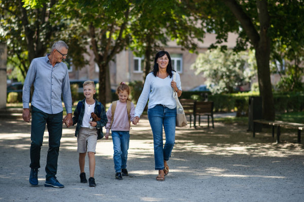 Happy grandparents taking grandchildren home from school, walking outdoors in a street.