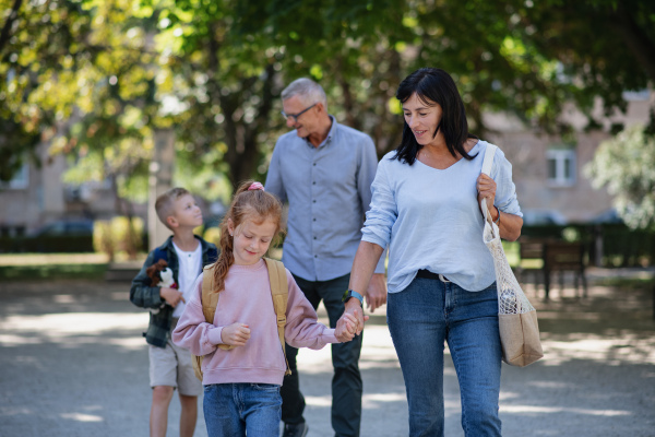 Happy grandparents taking grandchildren home from school, walking outdoors in a street.