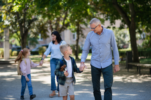 Happy grandparents taking grandchildren home from school, walking outdoors in a street.