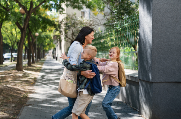 Happy schoolchildren running to their grandmother waiting for them after school outdoors in a street.