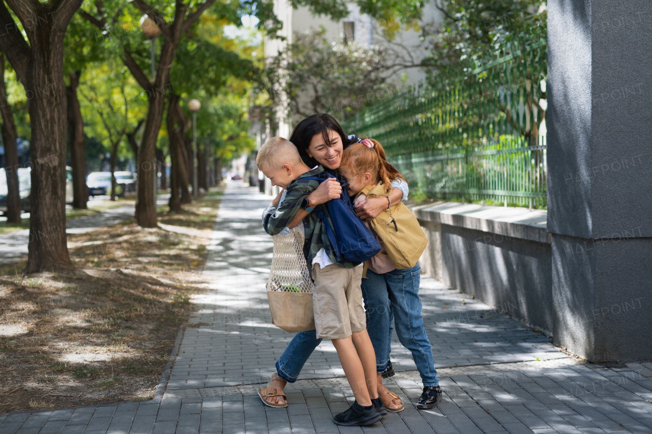 Happy schoolchildren hugging their grandmother waiting for her after school outdoors in a street.