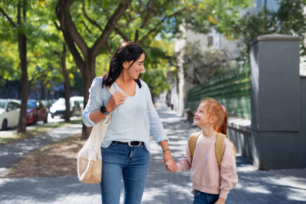 A happy grandmother taking granddaughter home from school, walking outdoors in street.