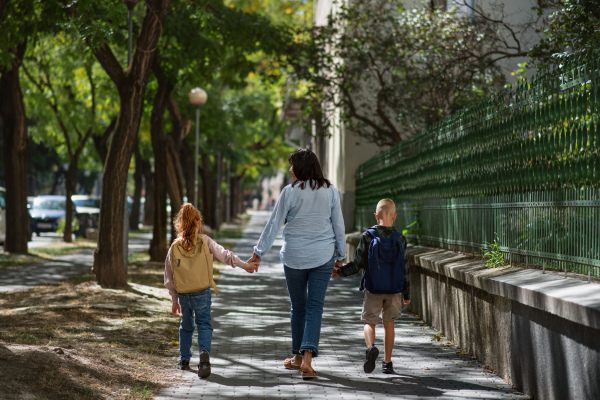 A rear view of happy grandmother taking grandchildren home from school, walking outdoors in street.