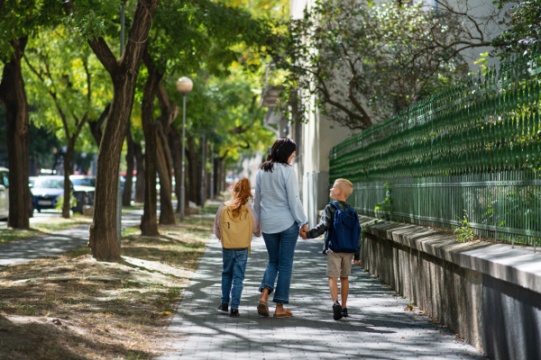 A rear view of grandmother taking grandchildren home from school, walking outdoors in street.