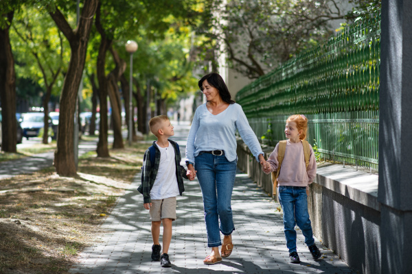 A happy grandmother taking grandchildren home from school, walking outdoors in street.