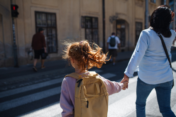 A rear view of grandmother with granddaughter crossing the street during sunset.