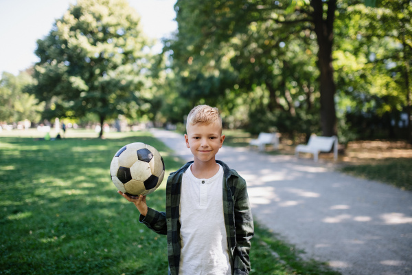 A happy little boy holding ball and looking at camera in park.