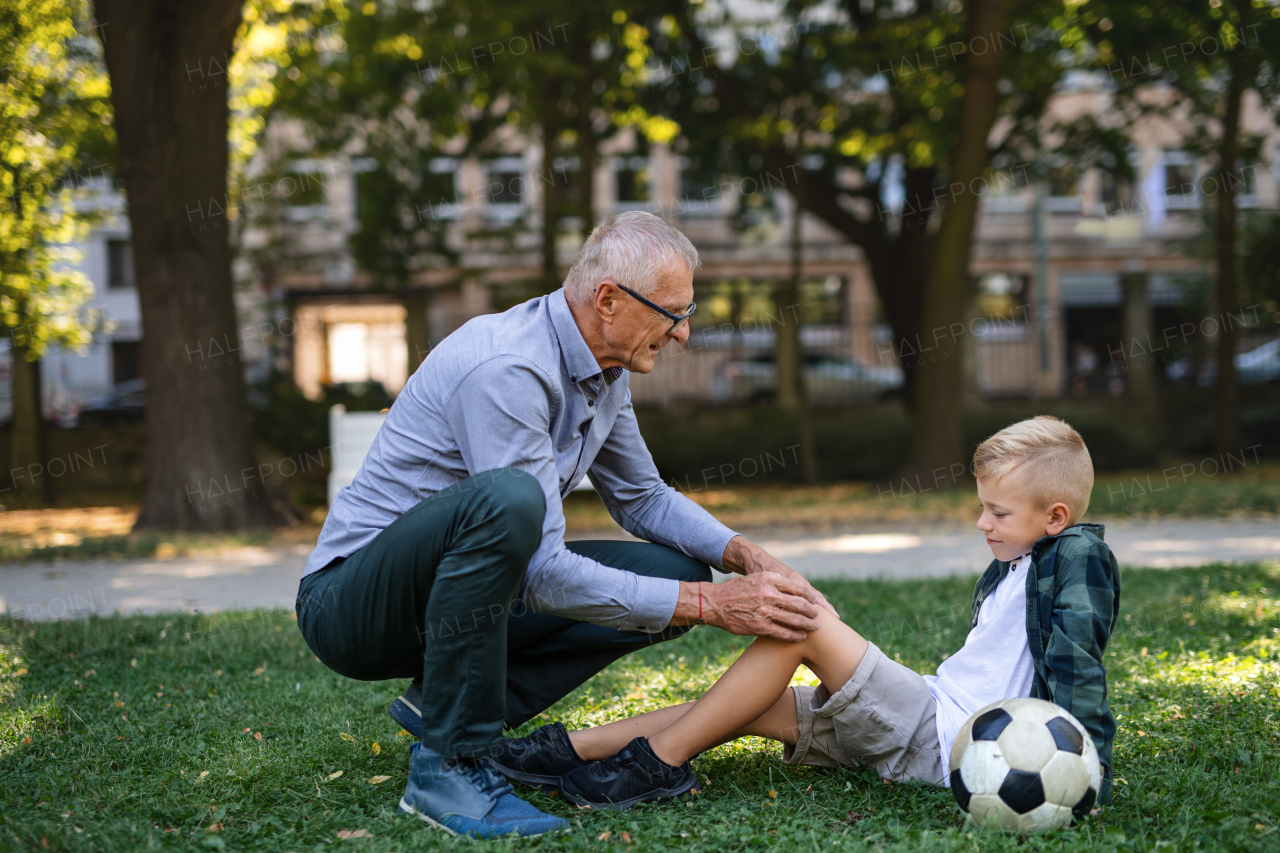 A little boy with injured leg getting plaster from grandfather outdoors in park.