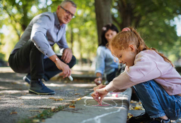 A senior couple with grandchildren drawing with chalks on pavement outdoors in park.