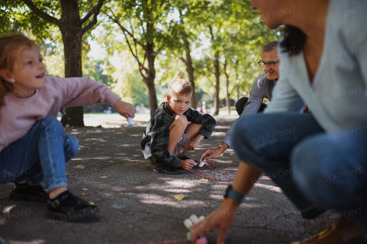 A senior couple with grandchildren drawing with chalks on pavement outdoors in park.