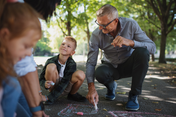 A senior couple with grandchildren drawing with chalks on pavement outdoors in park.