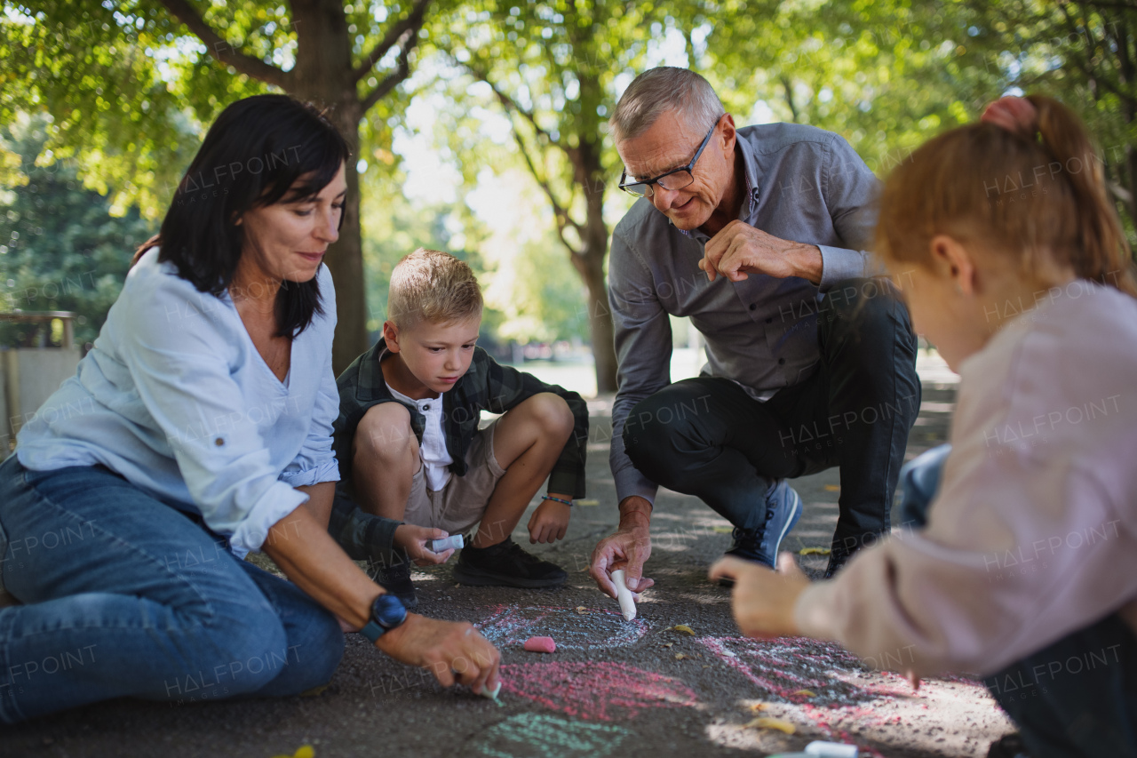 A senior couple with grandchildren drawing with chalks on pavement outdoors in park.